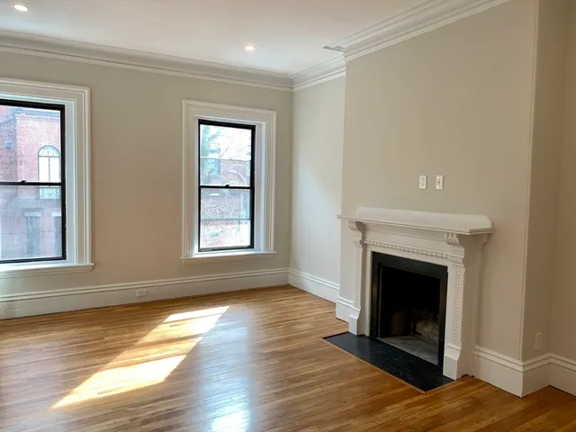 a view of an empty room with wooden floor fireplace and a window