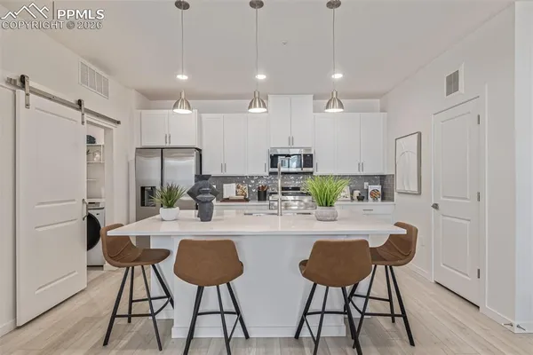 a kitchen with stainless steel appliances kitchen island a refrigerator and a dining table with wooden floor