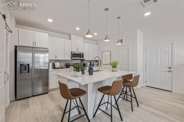 a kitchen with stainless steel appliances kitchen island granite countertop a refrigerator a stove a sink a dining table and chairs with wooden floor