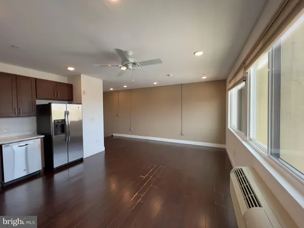 a view of an empty room with wooden floor and a kitchen