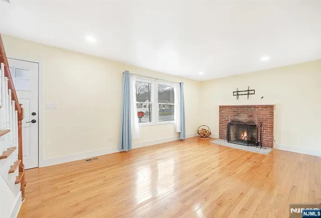 a view of an empty room with wooden floor fireplace and a window