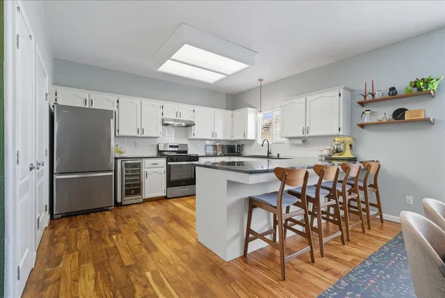 a kitchen with stainless steel appliances a refrigerator a stove a sink dishwasher and white cabinets with wooden floor