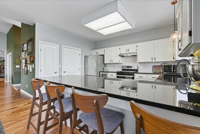 a kitchen with stainless steel appliances granite countertop a stove a sink dishwasher and white cabinets with wooden floor