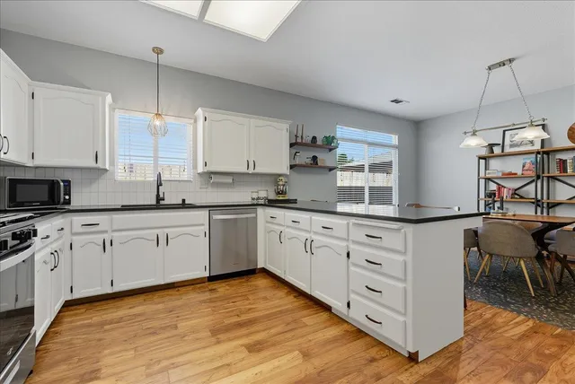 a kitchen with stainless steel appliances granite countertop a stove a sink dishwasher and white cabinets with wooden floor