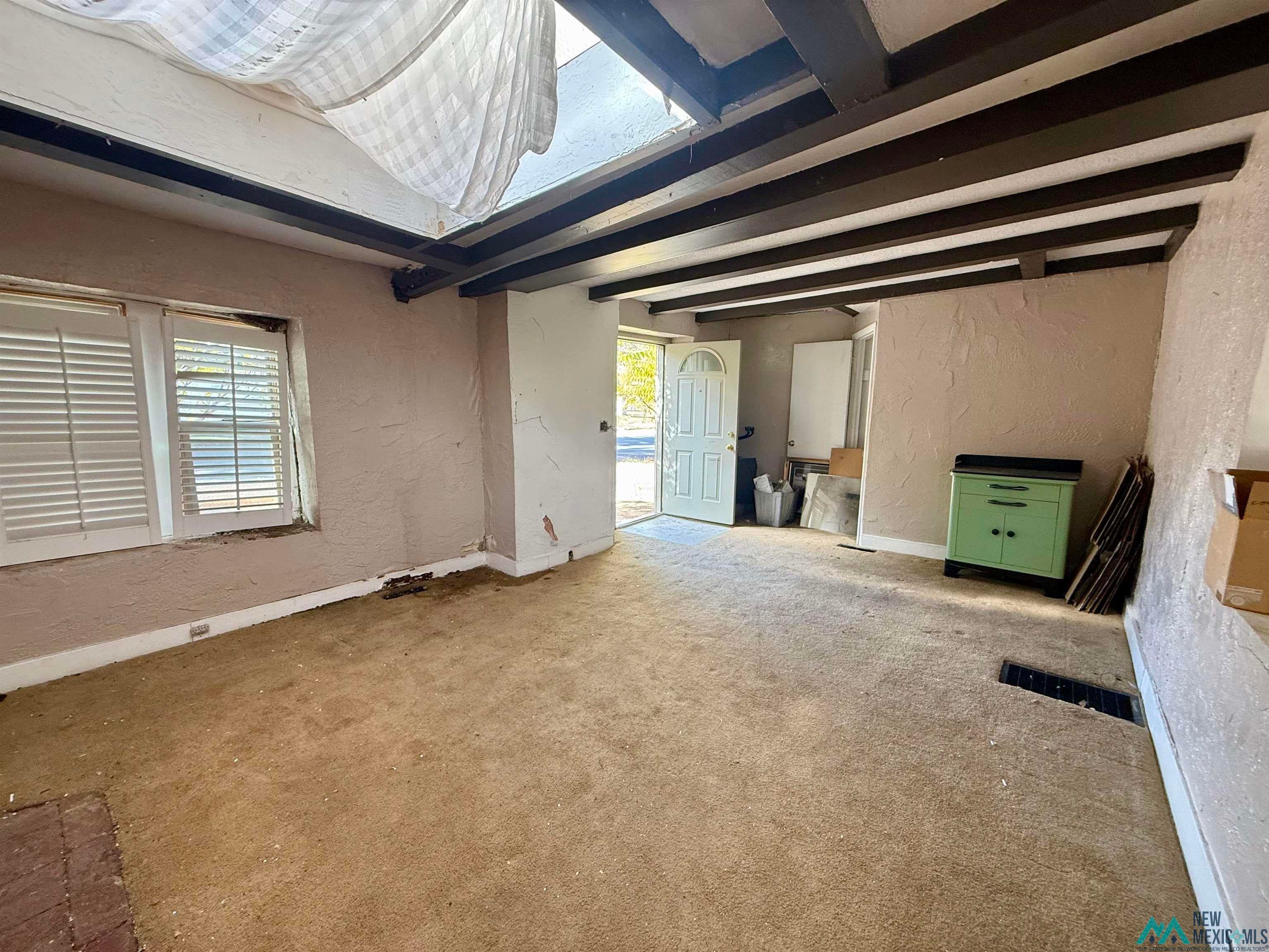 625 South 5th Street Raton, NM 87740 - Photo 9 of 45 Unfurnished living room featuring a textured wall, beamed ceiling, and carpet flooring
