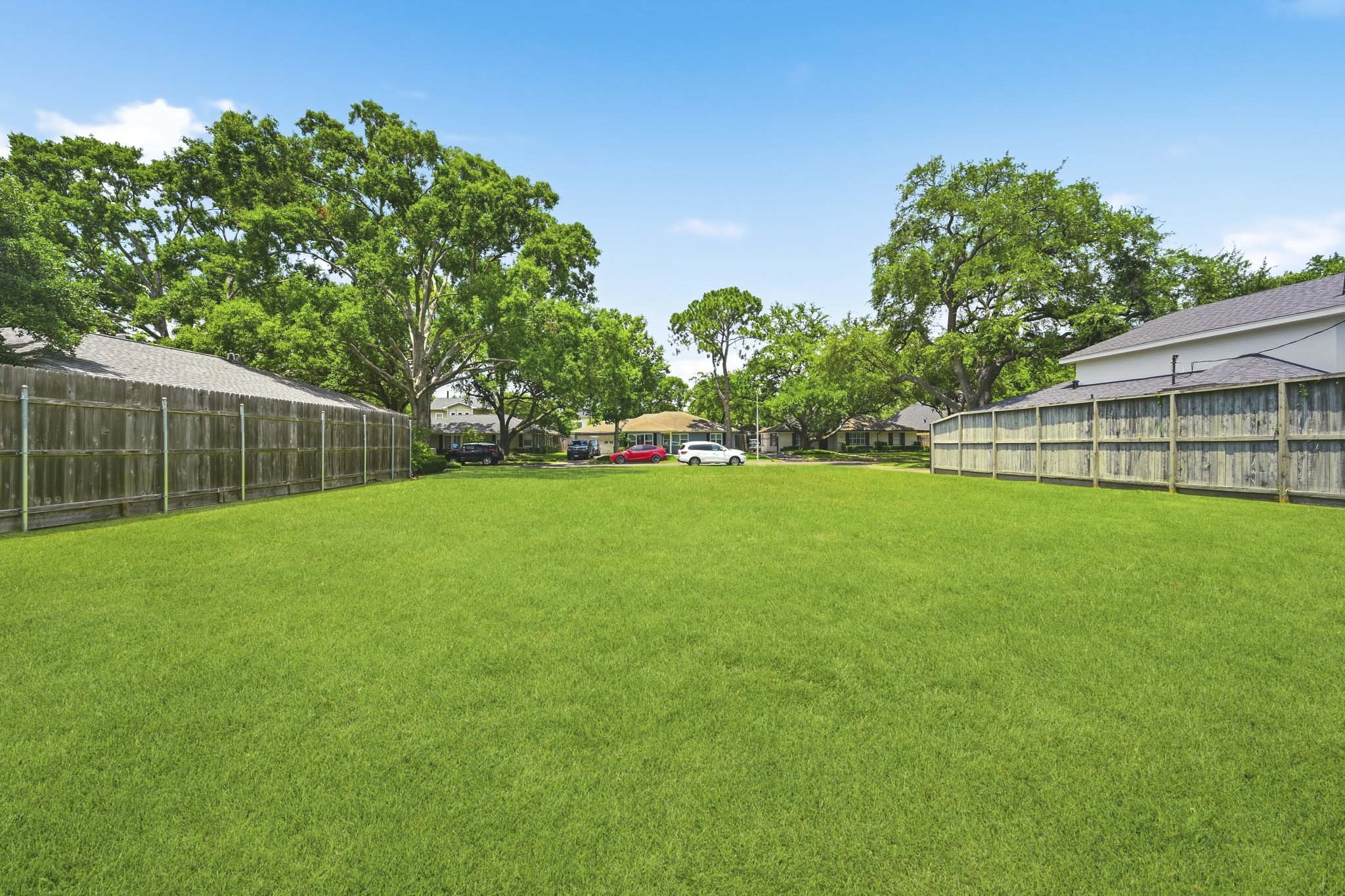 4227 Markham Street Houston, TX 77027 - Photo 3 of 7 Spacious, open grassy yard surrounded by wooden fences, with mature trees and neighboring houses in the background. Ideal for outdoor activities or potential landscaping.