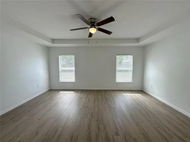 an empty room with wooden floor chandelier fan and windows