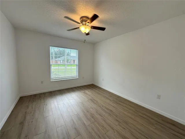 an empty room with wooden floor chandelier fan and windows