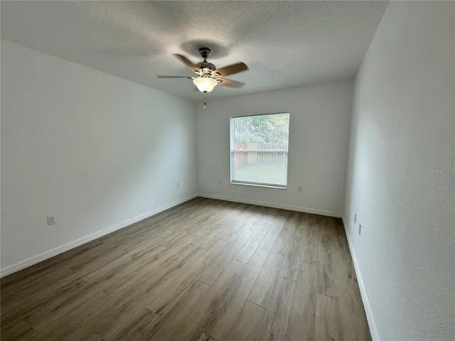 an empty room with wooden floor chandelier fan and windows