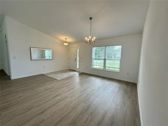 an empty room with wooden floor chandelier and windows