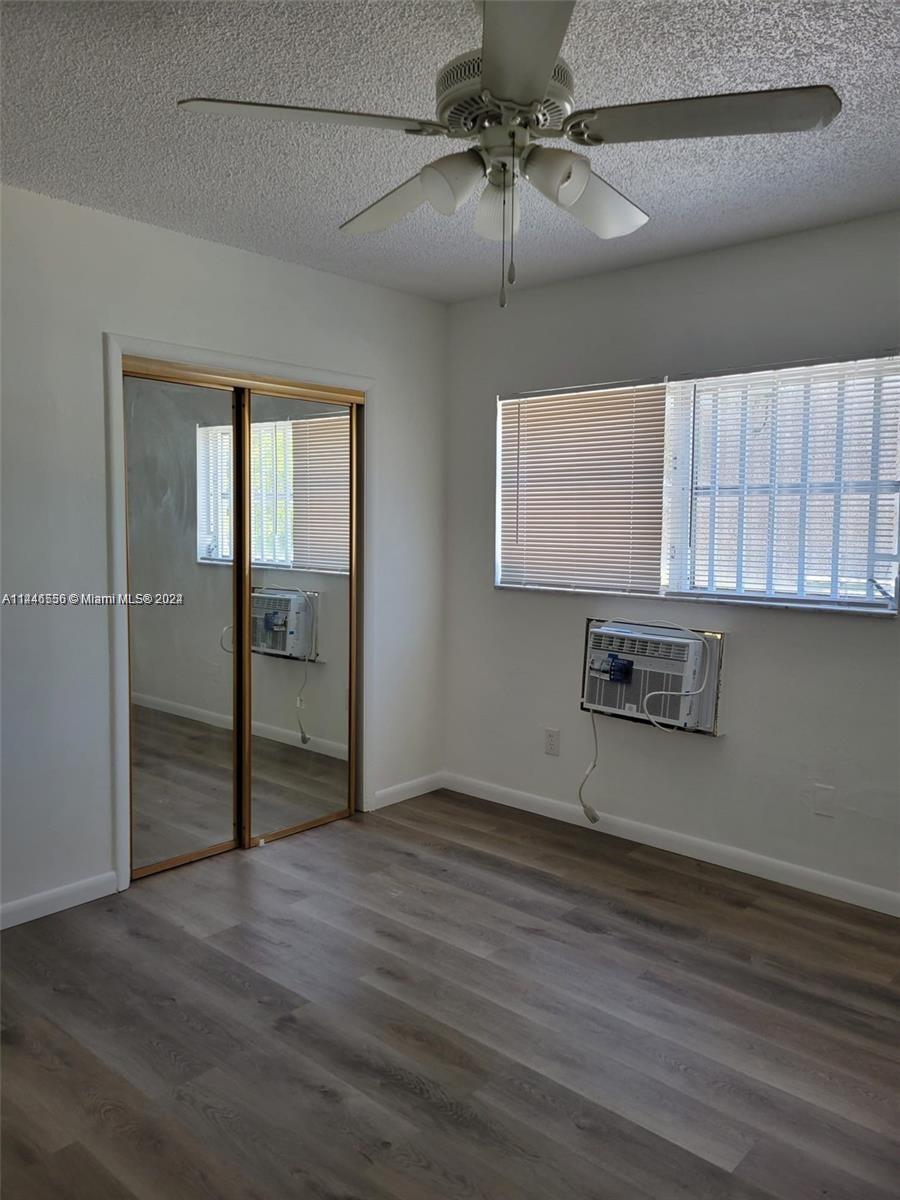 1755 Northeast 116th Road, Unit 9 North Miami, FL 33181 - Photo 13 of 27 an empty room with wooden floor chandelier fan and windows