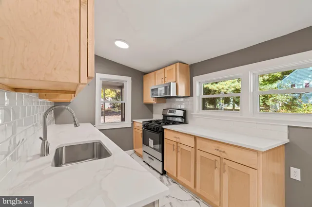 a kitchen with a sink a stove top oven a kitchen island a large window cabinets and stainless steel appliances