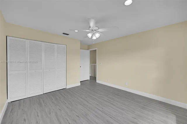 an empty room with wooden floor ceiling fan and window