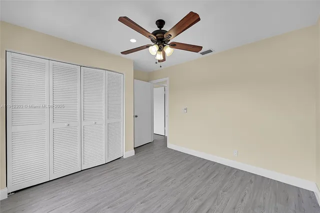an empty room with wooden floor ceiling fan and windows
