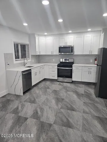 a large white kitchen with stainless steel appliances granite countertop a stove a sink a refrigerator and white cabinets