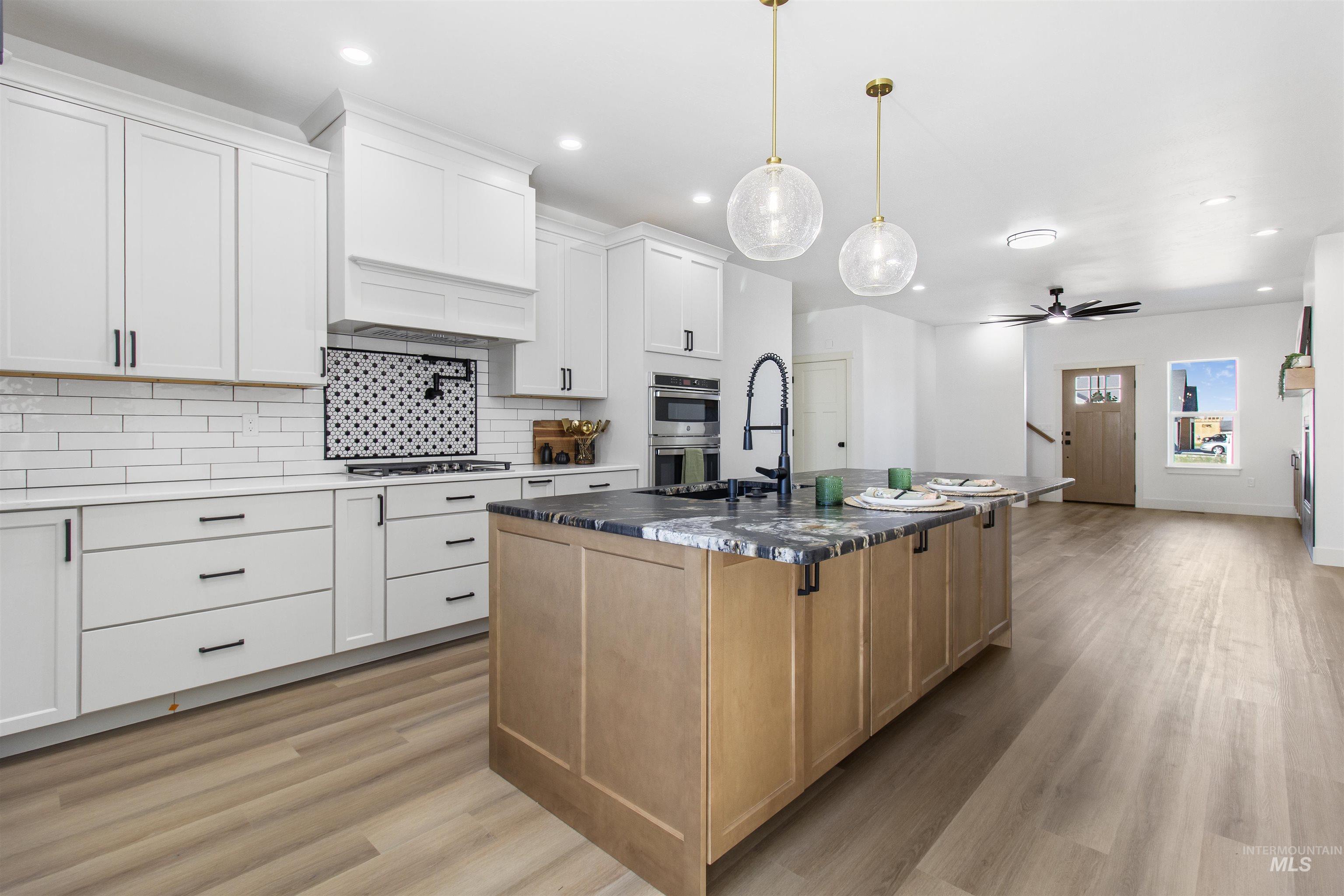 514 Full Moon Way Twin Falls, ID 83301 - Photo 12 of 49 Dual tone kitchen featuring dual tone cabinets, ceiling fan, light wood-style flooring, an island with sink, and dark stone countertops