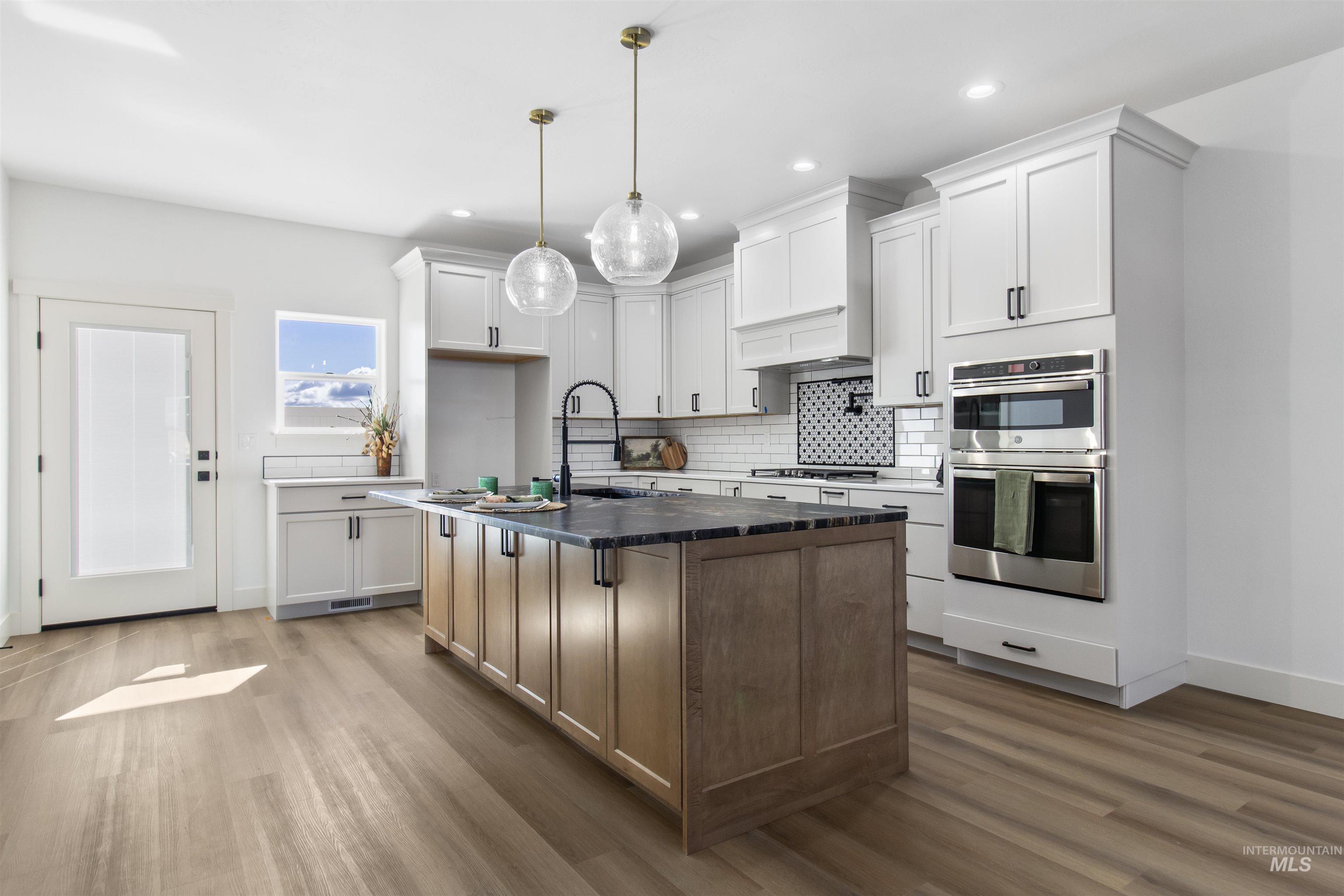 514 Full Moon Way Twin Falls, ID 83301 - Photo 8 of 49 Kitchen featuring a center island with sink, stainless steel appliances, dark wood-style floors, dual tone cabinets, and decorative light fixtures