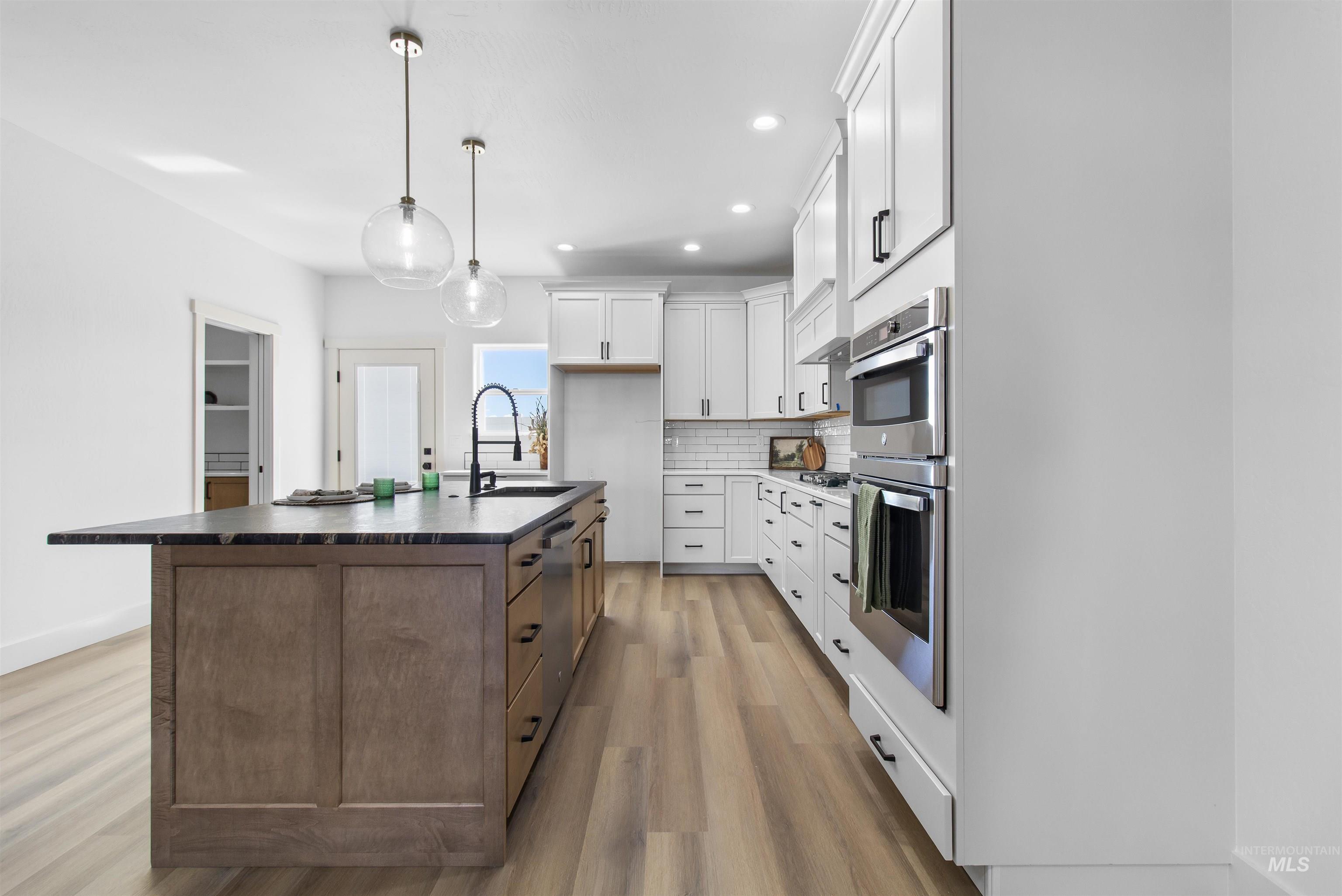 514 Full Moon Way Twin Falls, ID 83301 - Photo 9 of 49 Kitchen featuring two tone cabinetry, a kitchen island with sink, light wood finished floors, stainless steel appliances, and decorative backsplash