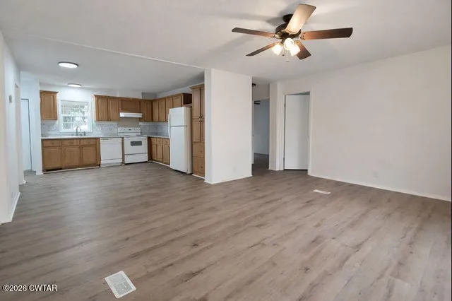 a view of a kitchen and an empty room with wooden floor