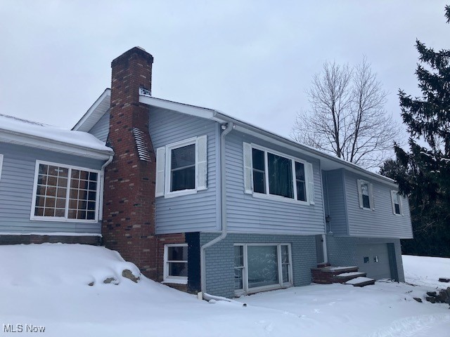14495 Peckham Road Burton, OH 44021 - Photo 1 of 24 View of snowy exterior with brick siding, a chimney, and an attached garage