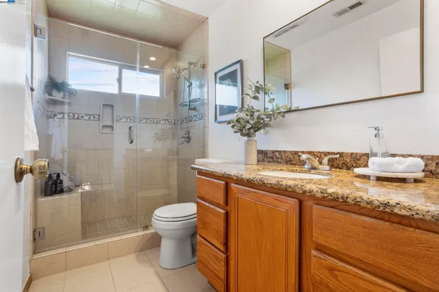 a bathroom with a granite countertop sink a toilet a mirror and shower