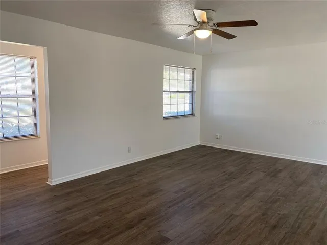 an empty room with wooden floor ceiling fan and windows