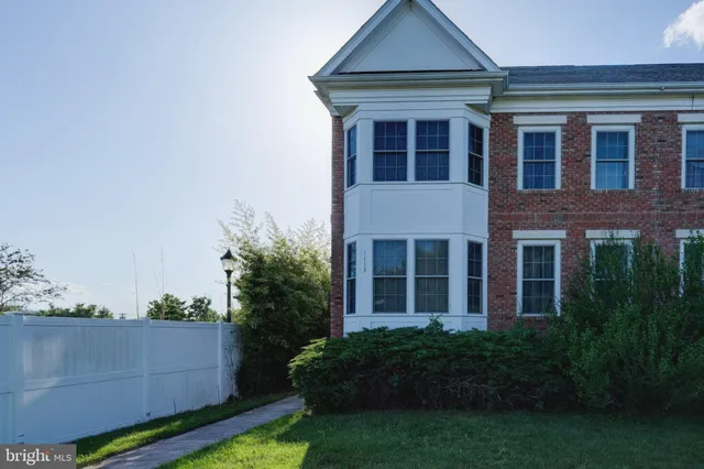 a view of a brick house with a yard plants and large tree