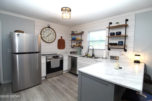 a kitchen with stainless steel appliances granite countertop a refrigerator a stove and a sink with wooden floor