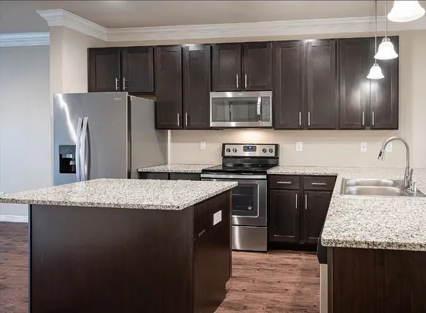 a kitchen with kitchen island granite countertop stainless steel appliances wooden cabinets a refrigerator and a sink