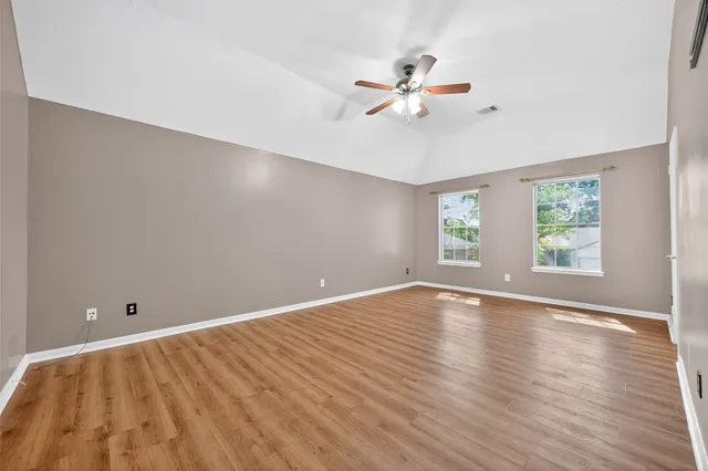 an empty room with wooden floor fan and windows