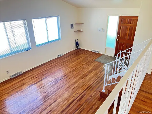 a view of an empty room with wooden floor and fan