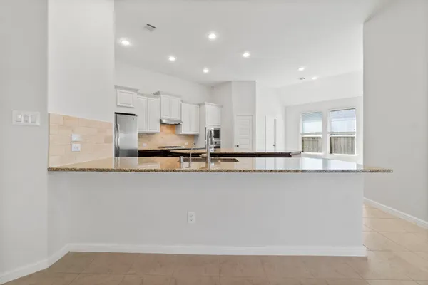 a large kitchen with stainless steel appliances granite countertop a stove a sink a refrigerator and white cabinets with wooden floor