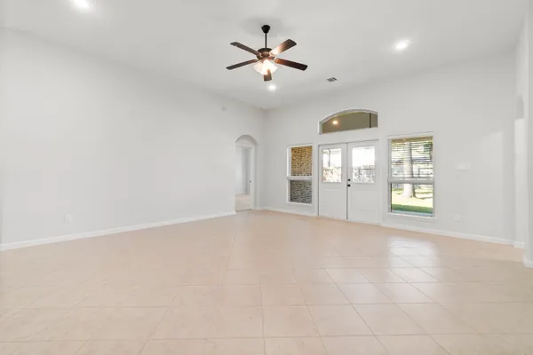 an empty room with chandelier fan and windows