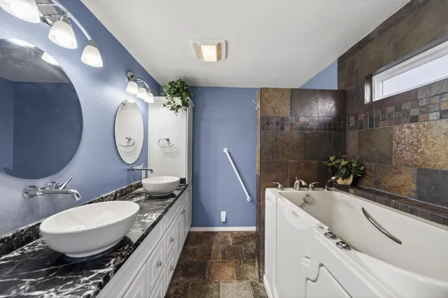 a bathroom with a granite countertop double vanity sink a mirror and a shower