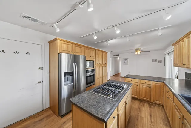 a kitchen with stainless steel appliances granite countertop a refrigerator a sink dishwasher a stove and a dining table with wooden floor