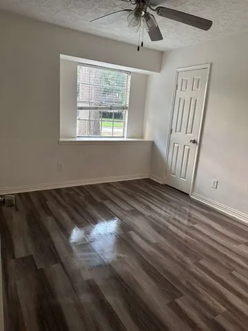 a view of an empty room with wooden floor and fan