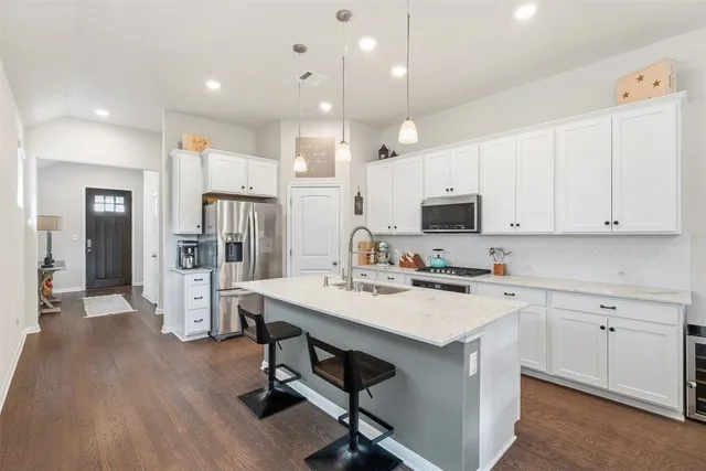 a kitchen with stainless steel appliances a stove a sink a refrigerator and white cabinets with wooden floor