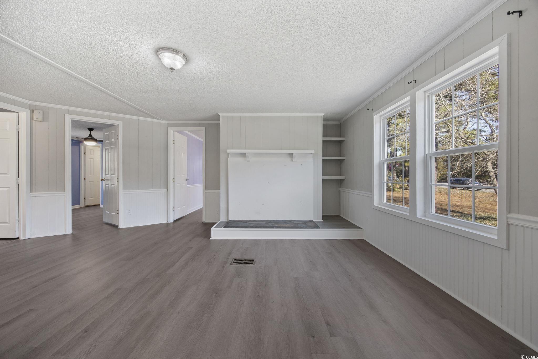 4221 Blake Road Myrtle Beach, SC 29588 - Photo 12 of 36 Unfurnished living room featuring wood walls, dark wood finished floors, a textured ceiling, crown molding, and a wainscoted wall
