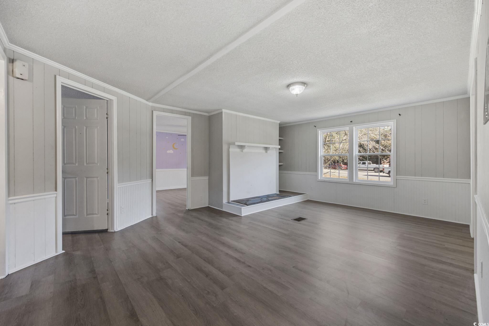 4221 Blake Road Myrtle Beach, SC 29588 - Photo 13 of 36 Unfurnished living room with dark wood finished floors, ornamental molding, wood walls, and a textured ceiling