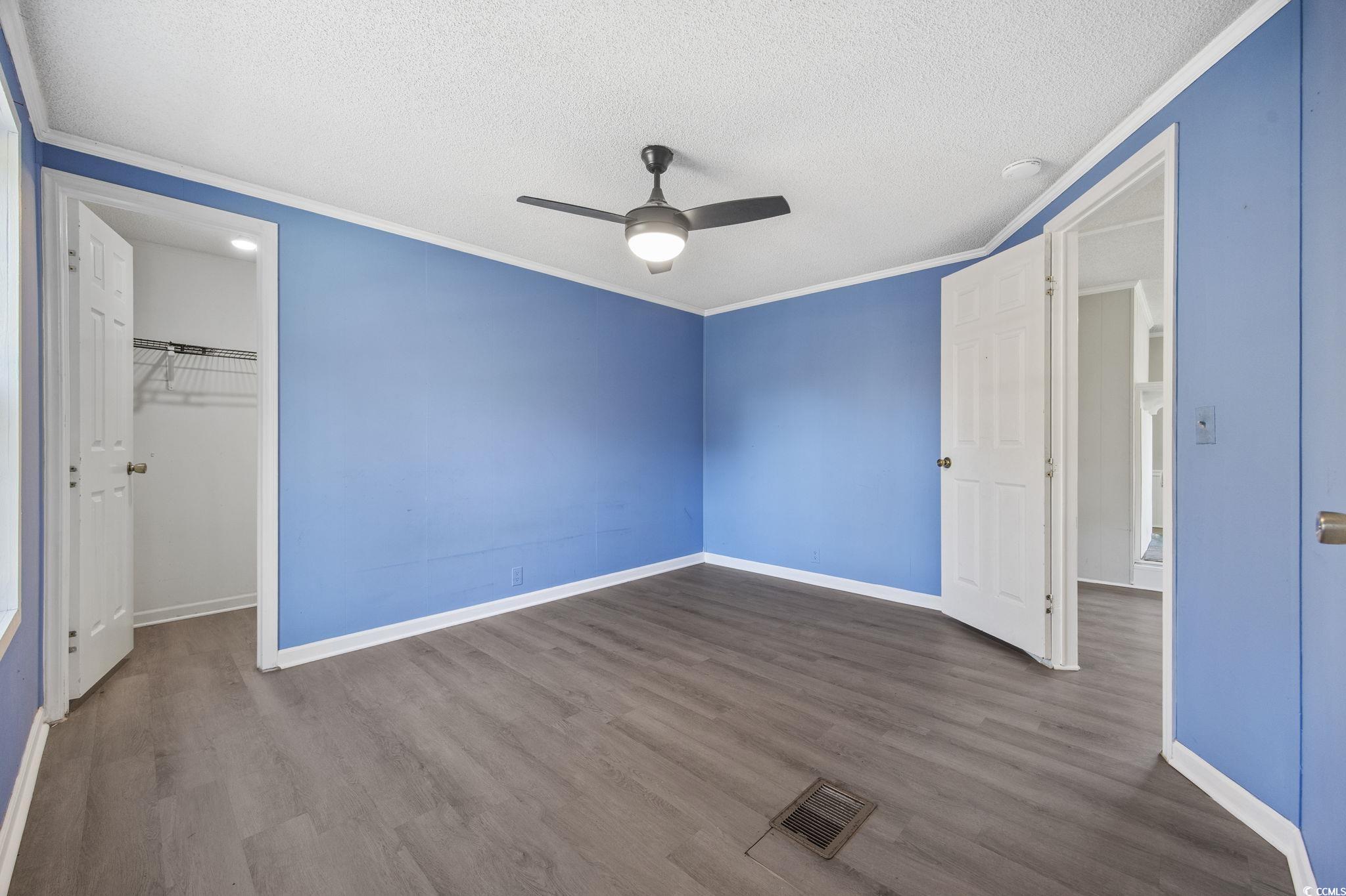 4221 Blake Road Myrtle Beach, SC 29588 - Photo 19 of 36 Unfurnished bedroom with ornamental molding, dark wood finished floors, a walk in closet, a textured ceiling, and a ceiling fan