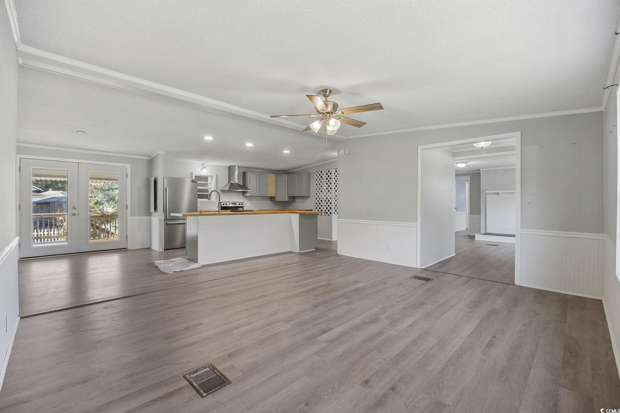 4221 Blake Road Myrtle Beach, SC 29588 - Photo 3 of 36 Unfurnished living room with ornamental molding, light wood-style flooring, ceiling fan, french doors, and wainscoting