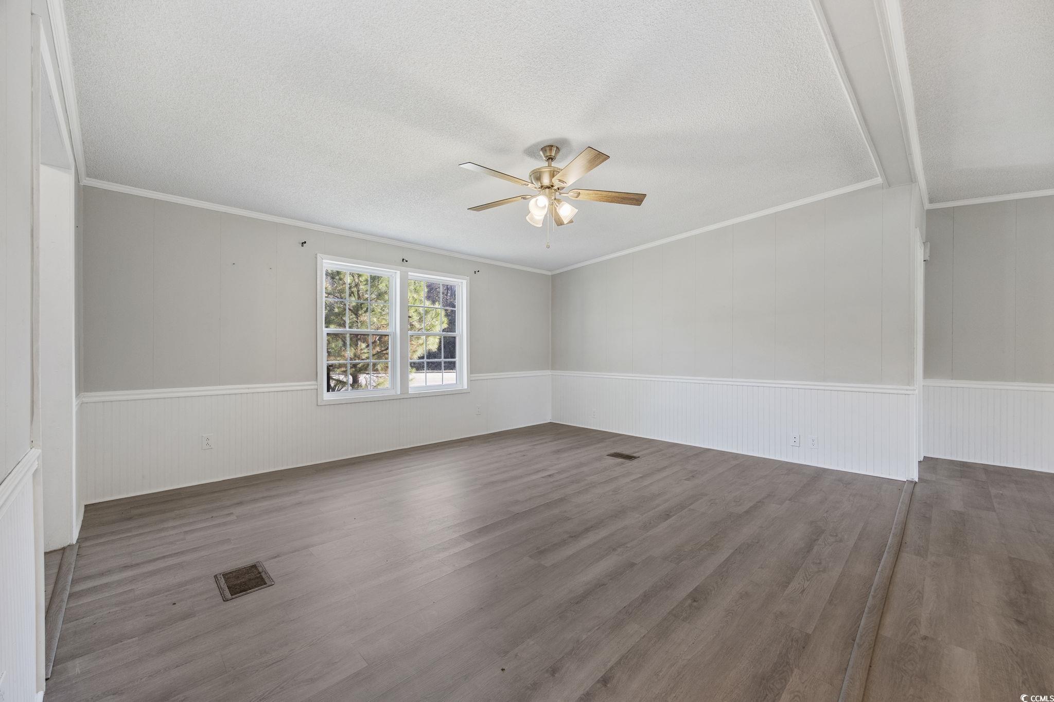 4221 Blake Road Myrtle Beach, SC 29588 - Photo 4 of 36 Spare room with wood finished floors, ceiling fan, crown molding, a textured ceiling, and a wainscoted wall