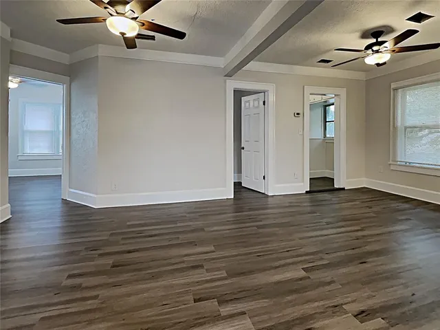 a view of an empty room with wooden floor and a ceiling fan