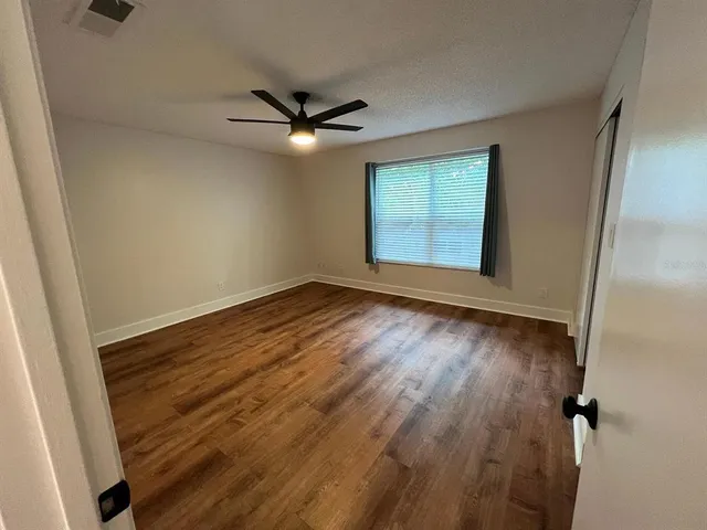 an empty room with wooden floor fan and windows