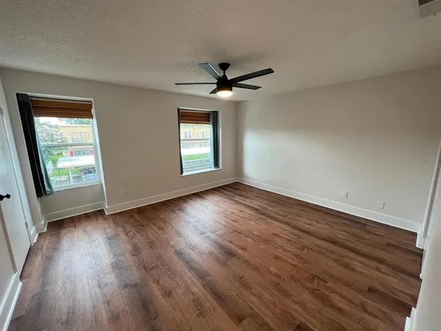 an empty room with wooden floor chandelier fan and windows