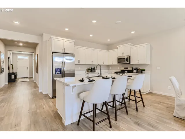 a kitchen with stainless steel appliances kitchen island granite countertop a refrigerator a stove a sink dishwasher and a dining table with wooden floor