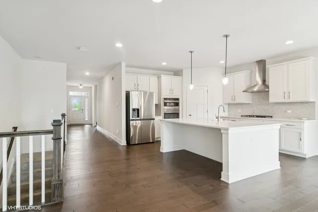 a kitchen with stainless steel appliances kitchen island granite countertop a stove a sink a refrigerator and white cabinets with wooden floor