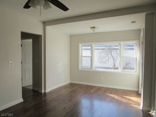 an empty room with wooden floor chandelier fan and windows