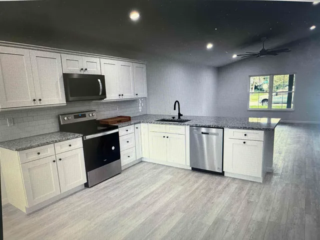 a kitchen with stainless steel appliances granite countertop a sink a stove top oven a refrigerator with white cabinets and wooden floor