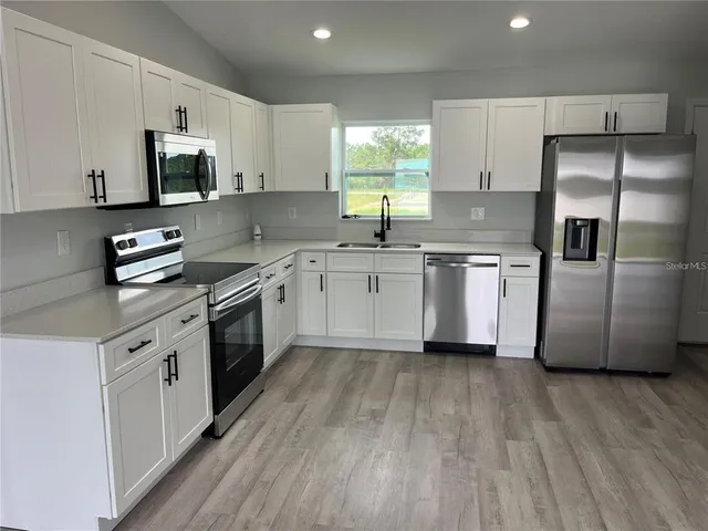 a kitchen with stainless steel appliances a sink dishwasher a refrigerator and a stove with wooden floors